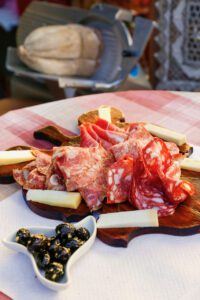 A wooden platter with cured meats, cheese, and olives from a Tuscany farm, served on a checkered tablecloth.