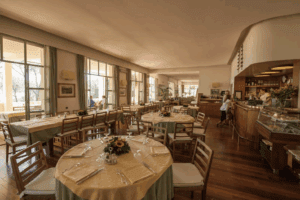 A cozy clubhouse dining room with round tables set with floral centerpieces, cutlery, and glasses, featuring large windows and a wooden interior.