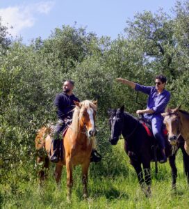 Group of people on horseback in a Tuscan olive grove, with one rider pointing ahead during a guided Tuscany horseback ride.