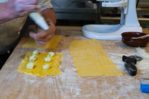 A chef filling yellow pasta dough with ricotta and spinach on a floured surface, hands dusted with flour.