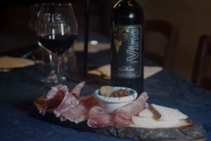 A bottle of red wine beside a platter with slices of ham and cheese, set on a table for a gourmet experience.