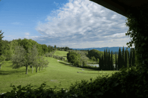 A vibrant green Tuscany golf field with a golf ball and club resting on the grass, showcasing the natural landscape.