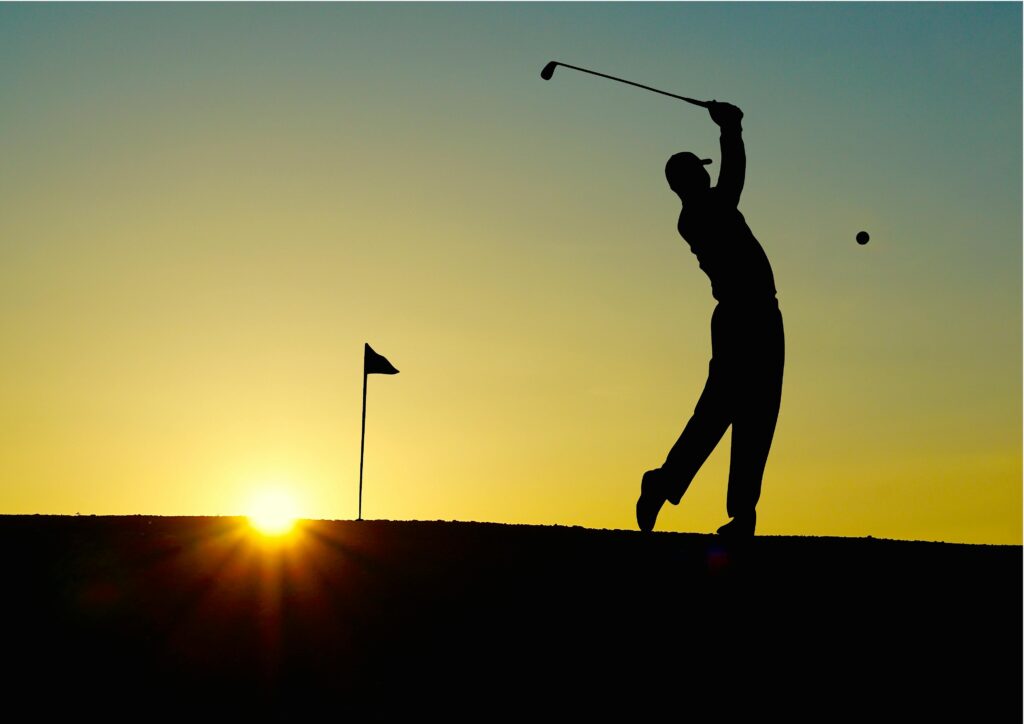 Golfer in Action at Tuscany Sunset A young golfer in a white polo and beige pants hitting a golf ball on a lush green field in Tuscany under a vibrant sunset.