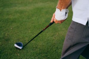 A golfer in a white polo and short gray pants preparing to hit a golf ball with a club on a lush green Tuscany field.