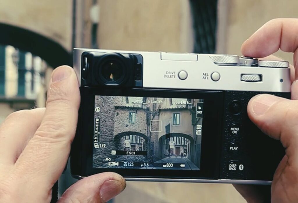 Image 1 — Hands holding a Fujifilm camera in multiple exposure mode framing a Florence archway during a double exposure photography Florence photo walk