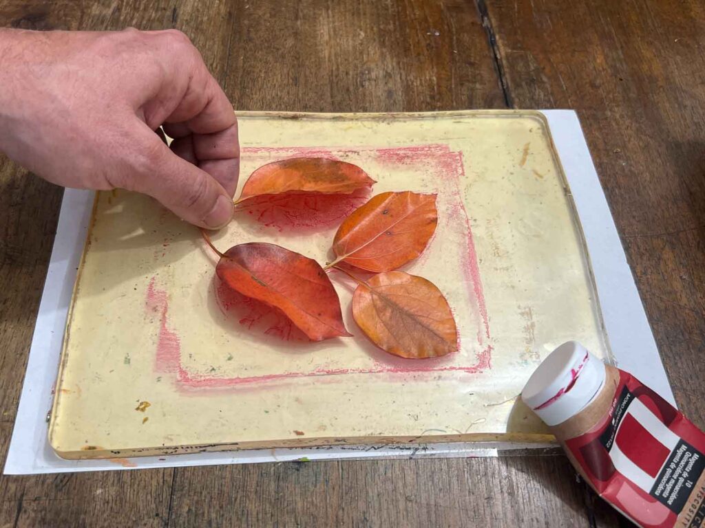 Hands positioning autumn leaves on the gel plate during an art workshop for kids Florence at Fatacadabra