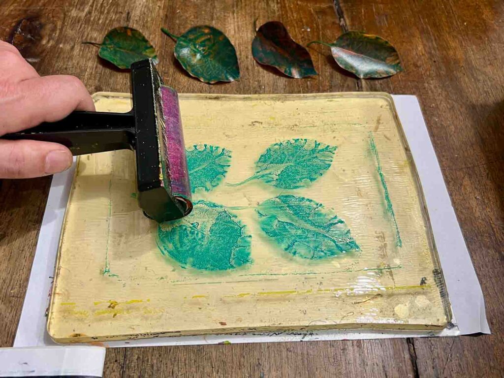 Rolling teal acrylic over leaf impressions on the gel plate at a gel plate printing Florence session