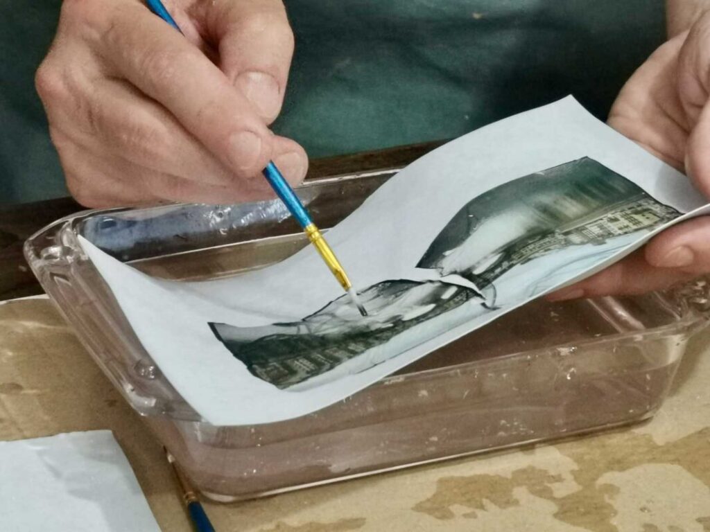 Lifting a Polaroid emulsion from its backing with a brush in warm water at a Polaroid emulsion lift Florence workshop
