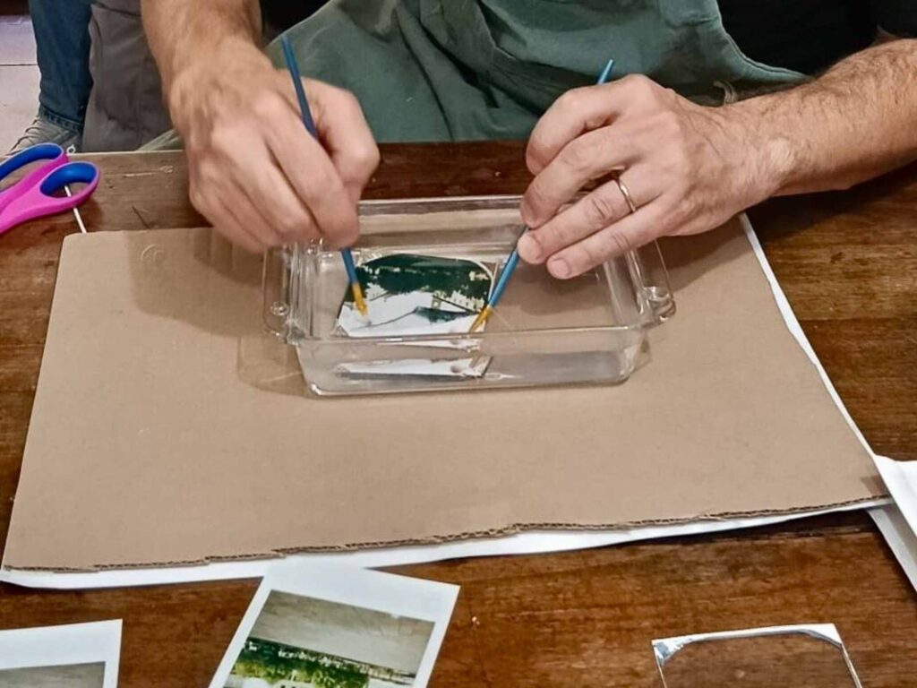 Two people using brushes to separate a Polaroid emulsion in a water dish at a Polaroid workshop Florence, Fatacadabra