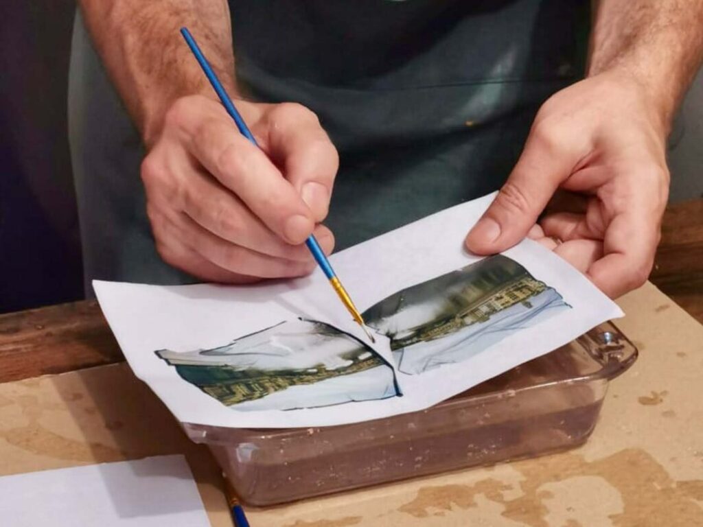 Hands carefully peeling a Polaroid emulsion from its white support during the Polaroid emulsion lift Florence session