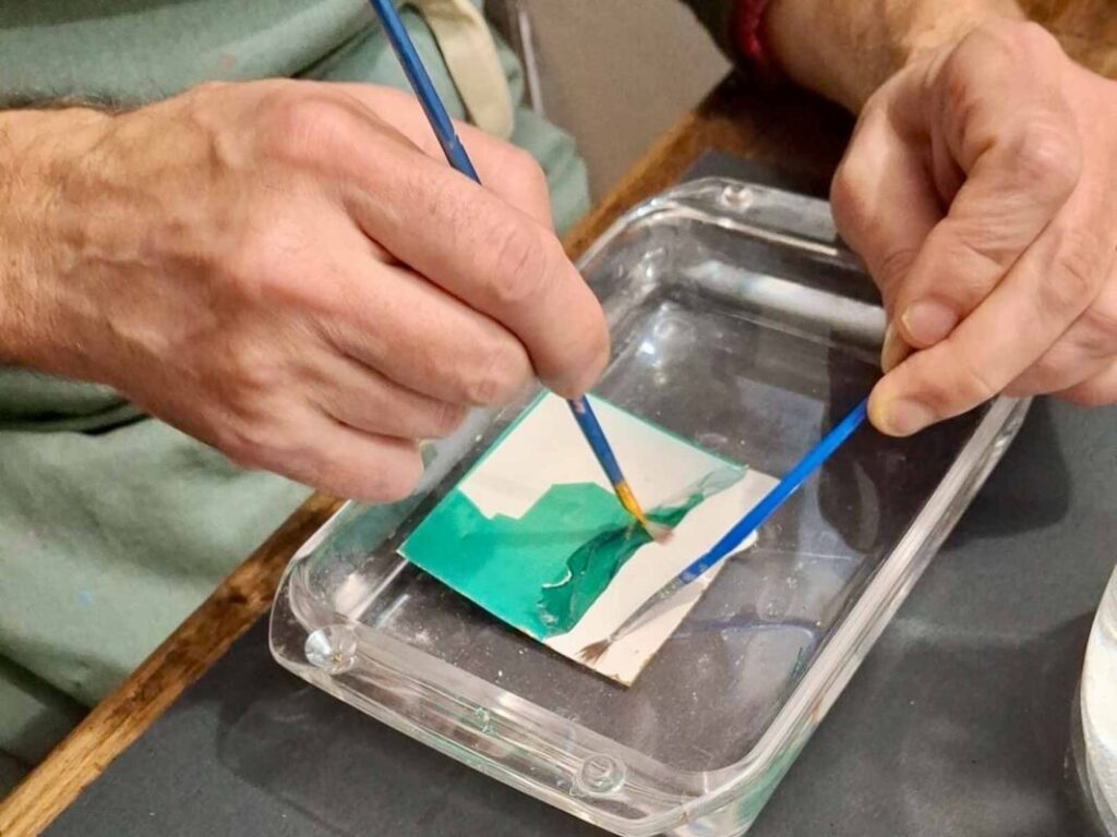Close-up of hands separating a teal Polaroid emulsion in water at a creative workshop Florence, Fatacadabra