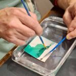 Close-up of hands separating a teal Polaroid emulsion in water at a creative workshop Florence, Fatacadabra