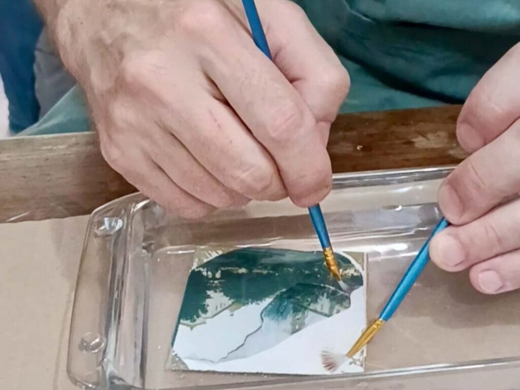 Two brushes carefully working a Polaroid emulsion in water at an analogue photography Florence workshop