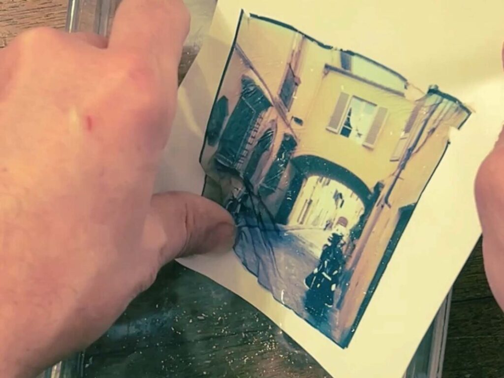 Hands transferring a Polaroid emulsion image of a Florence street scene to watercolor paper