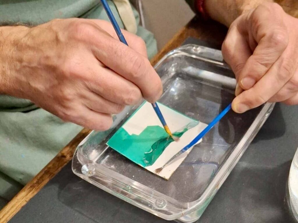 Close-up of two brushes separating a Polaroid emulsion in water at a Tuscany photography workshop, Fatacadabra