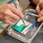 Close-up of two brushes separating a Polaroid emulsion in water at a Tuscany photography workshop, Fatacadabra