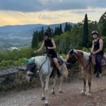 two riders on horseback at sunset overlooking Tuscan countryside