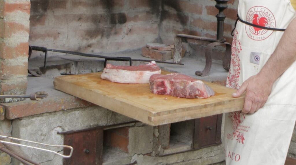 Local specialist preparing bistecca alla Fiorentina at a stone fireplace during a bistecca alla fiorentina experience at a Chianti winery near Florence.
