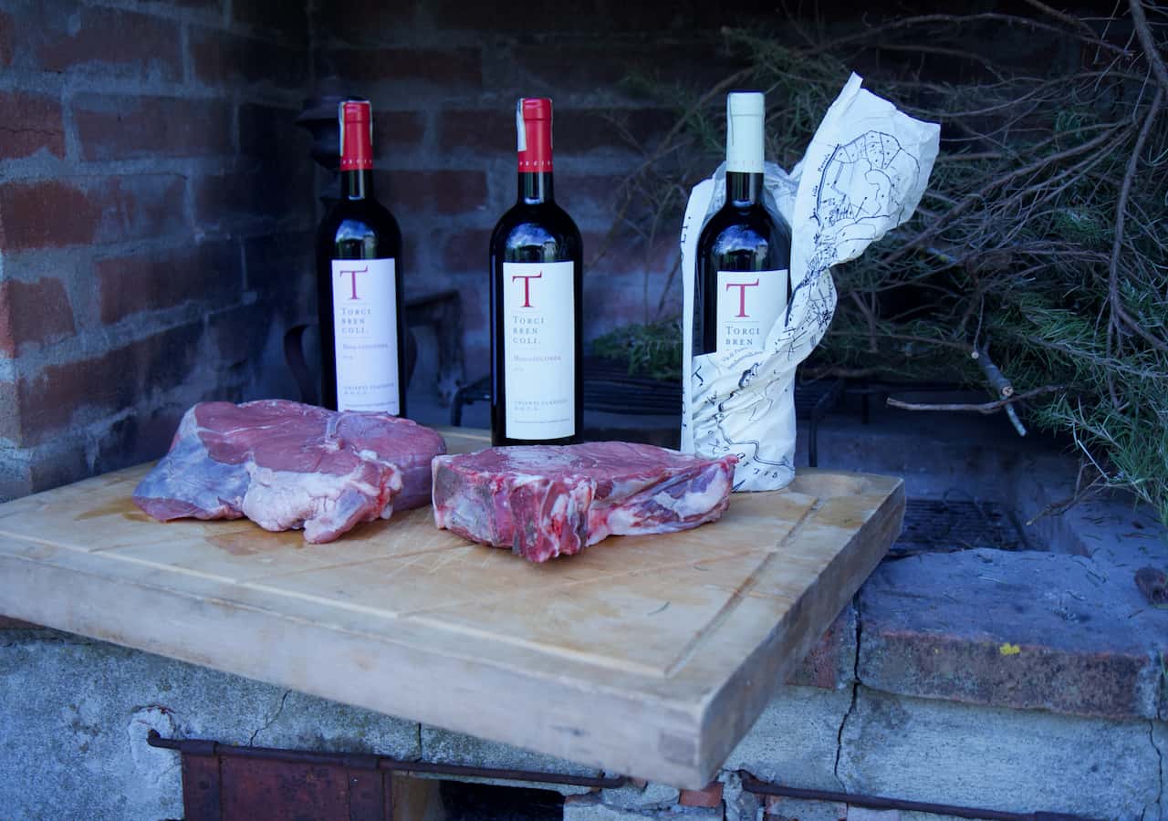Thick cuts of bistecca alla Fiorentina and Chianti Classico bottles at Torci Brencoli winery, part of a bistecca alla fiorentina experience on a private wine tour tuscany.