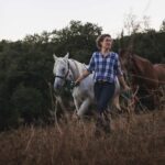 Horse guide Margherita walking a white and a chestnut horse through a dry Tuscan field — horseback riding in Italy