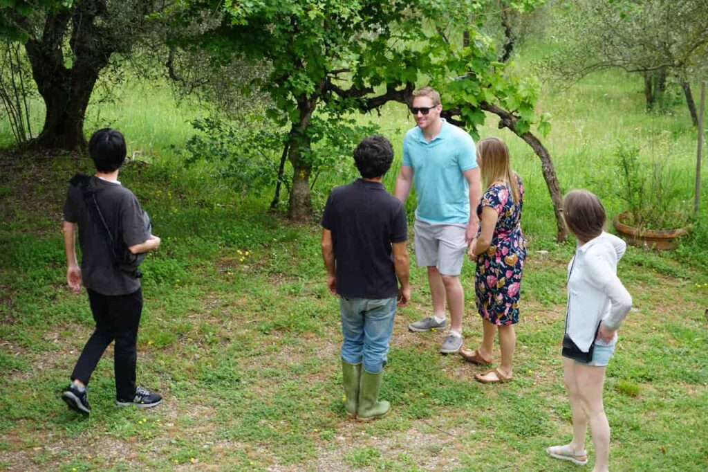 Small private group with a local producer in a Chianti garden during a wine tasting near florence, with olive trees and open countryside surrounding them.