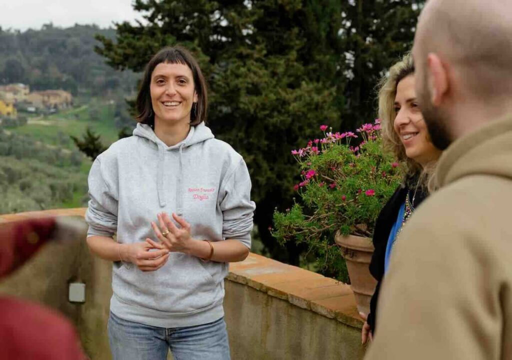 Local guide welcoming a small group on the terrace of a Chianti estate during a private wine tour tuscany, with rolling hills in the background.