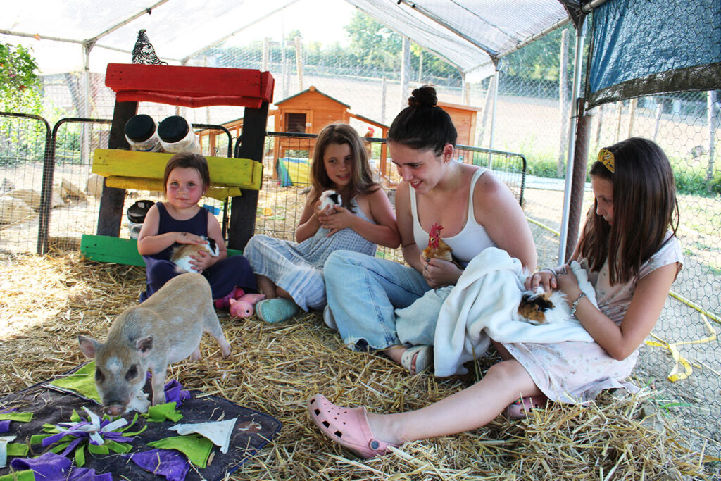 Young girls and a farm guide holding guinea pigs and a chicken on straw, a cooking class with kids Tuscany pairs with farm time.