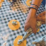 Hands piping green ravioli filling onto pasta circles on a checkered cloth, a cooking class with kids Tuscany can join.