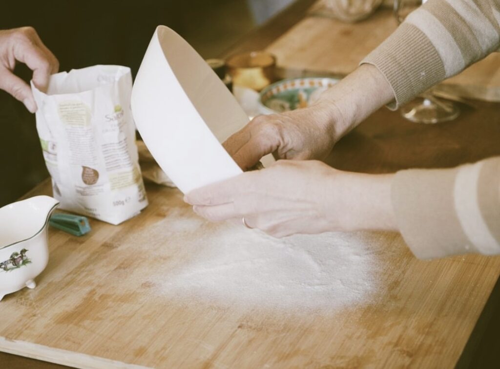 Hands pouring flour onto a wooden board to begin pasta dough on a family cooking class Tuscany.