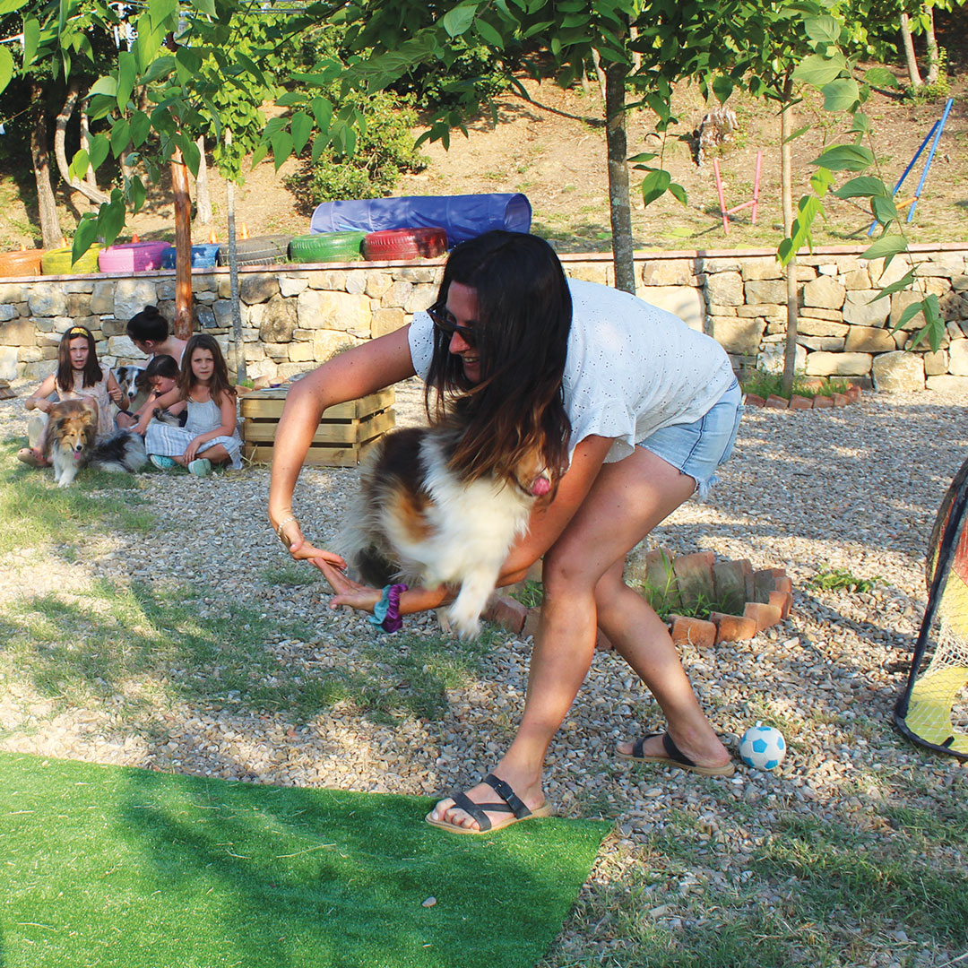 Woman playing with a fluffy farm dog as children look on, one of the family activities Tuscany evenings include.