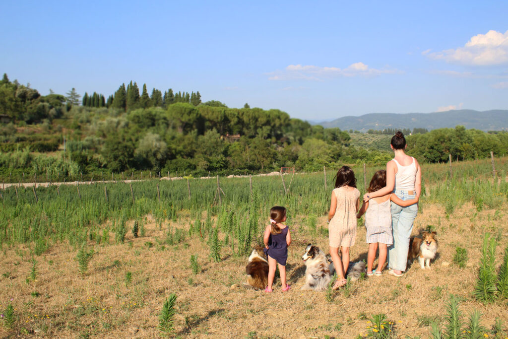 Woman and three children with farm dogs looking over green Tuscan fields, an evening of Tuscany with kids in the countryside.