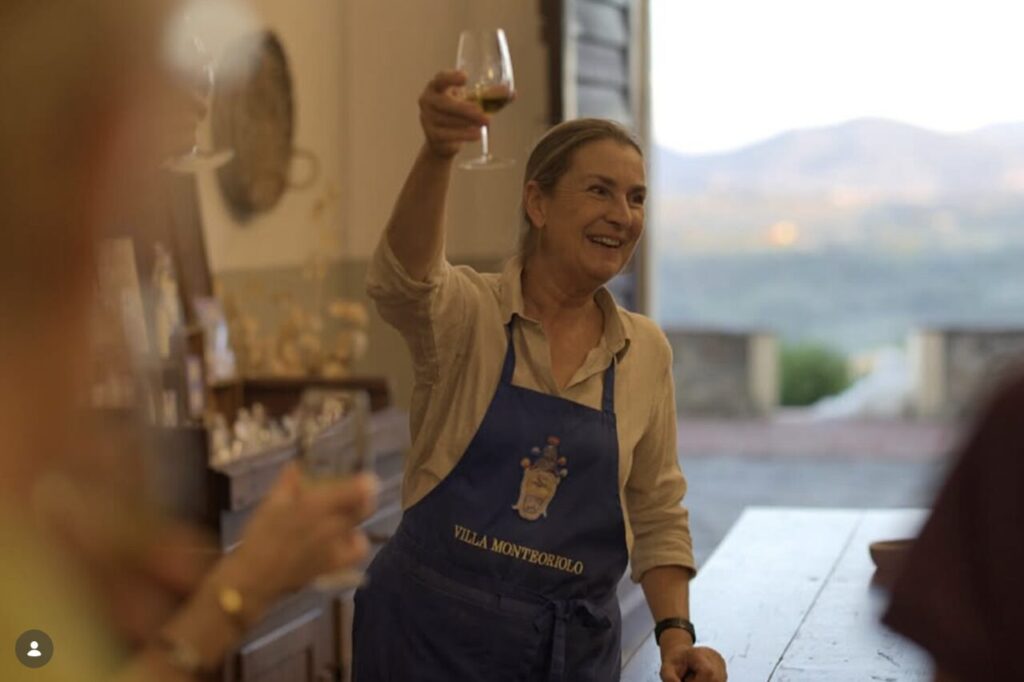 Woman in a Villa Monteoriolo apron raising a wine glass at the estate, the welcome toast on a family cooking class Tuscany.